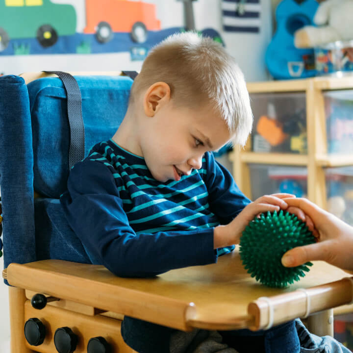 boy with Cerebral Palsy in special chair touches sensory ball